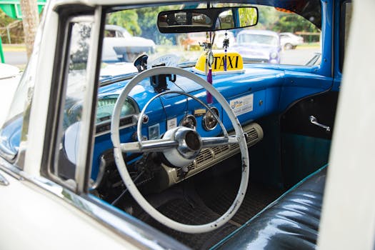 Interior of aged transport with steering wheel and leather seat under mirror reflecting town in daylight