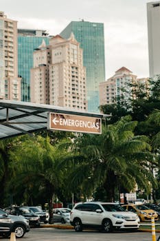 Vertical shot of cityscape featuring high-rise buildings, parked cars, and an emergency sign.