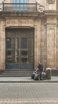 Worker arranging trash bags outside historic urban building Nacional Financiera.